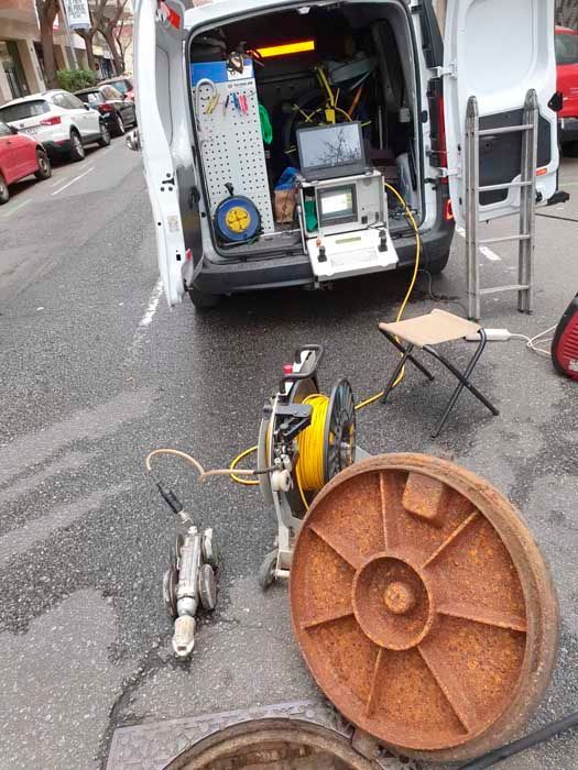 Una camioneta blanca estacionada en una calle con las puertas traseras abiertas. Cerca hay un equipo de inspección de alcantarillado.
