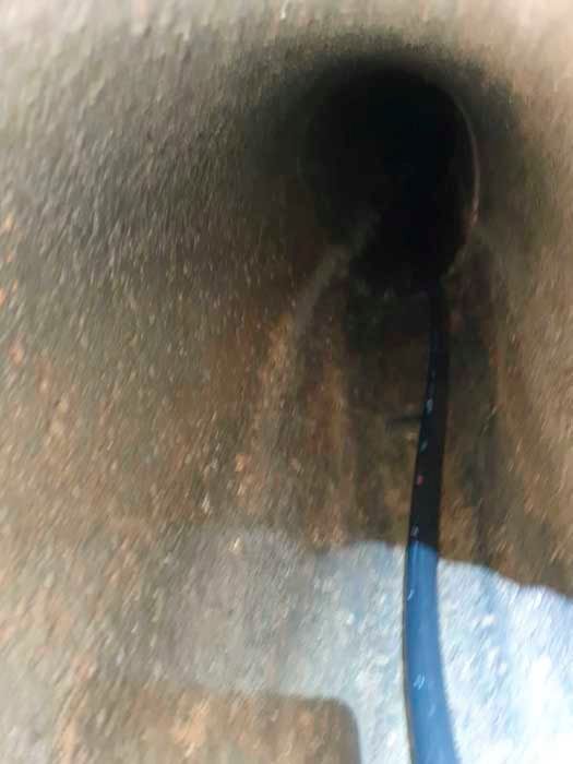 Interior de túnel oscuro con una manguera azul que desciende hacia la oscuridad.