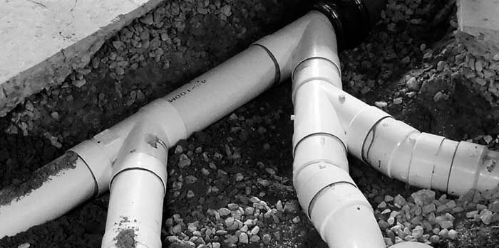 Tuberías y accesorios de PVC blanco en zanja, conectados a un sistema de drenaje.