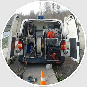 Furgoneta blanca con las puertas abiertas, llena de equipo. Se ven un generador y carretes de cable.