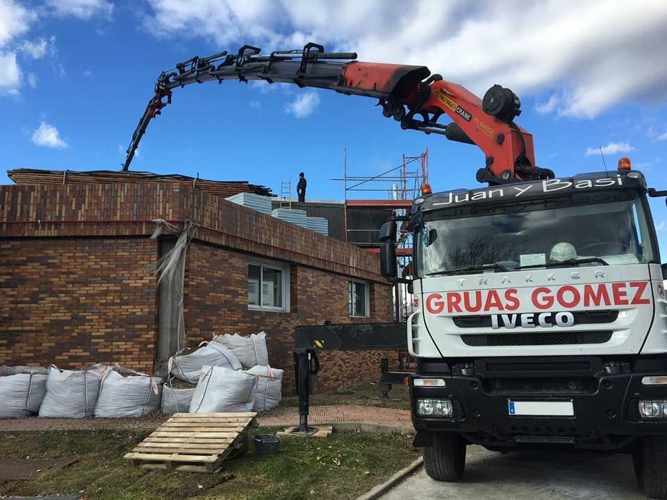 Un camión de Gruas Gómez está estacionado frente a un edificio de ladrillos.