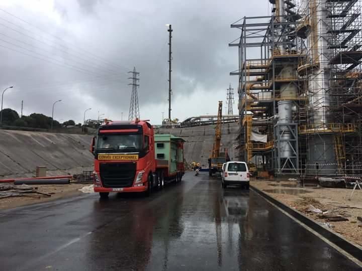 Un camión rojo circula por una carretera mojada frente a un edificio en construcción.