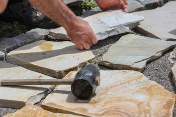Naturstein Platten im Außenbereich mit einem Hammer und jemanden der die Steine verlegt
