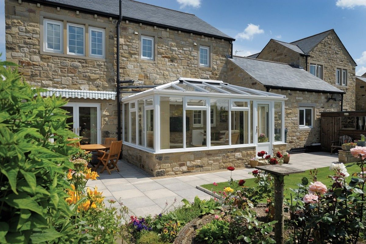 A stone house with a white conservatory in the backyard.
