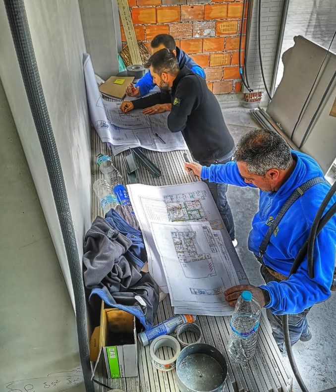 Tres personas vestidas de azul estudian planos en una obra en construcción.