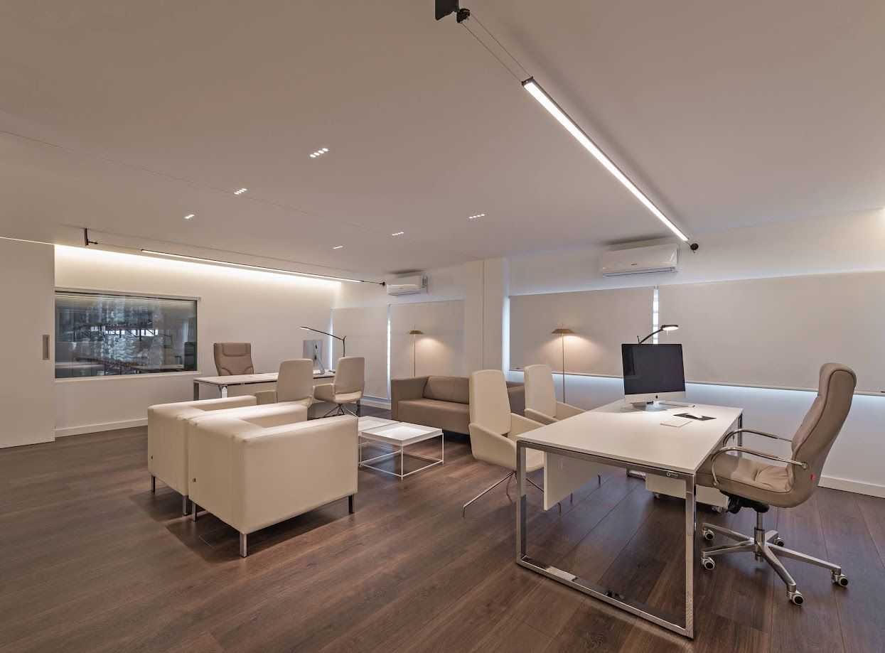 Interior de oficina moderno con paredes blancas, pisos de madera oscura, escritorios y asientos.