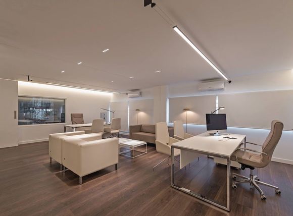 Interior de oficina moderno con paredes blancas, pisos de madera oscura, escritorios y asientos.