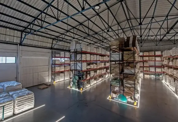 Interior de almacén con filas de estantes apilados llenos de productos envasados.