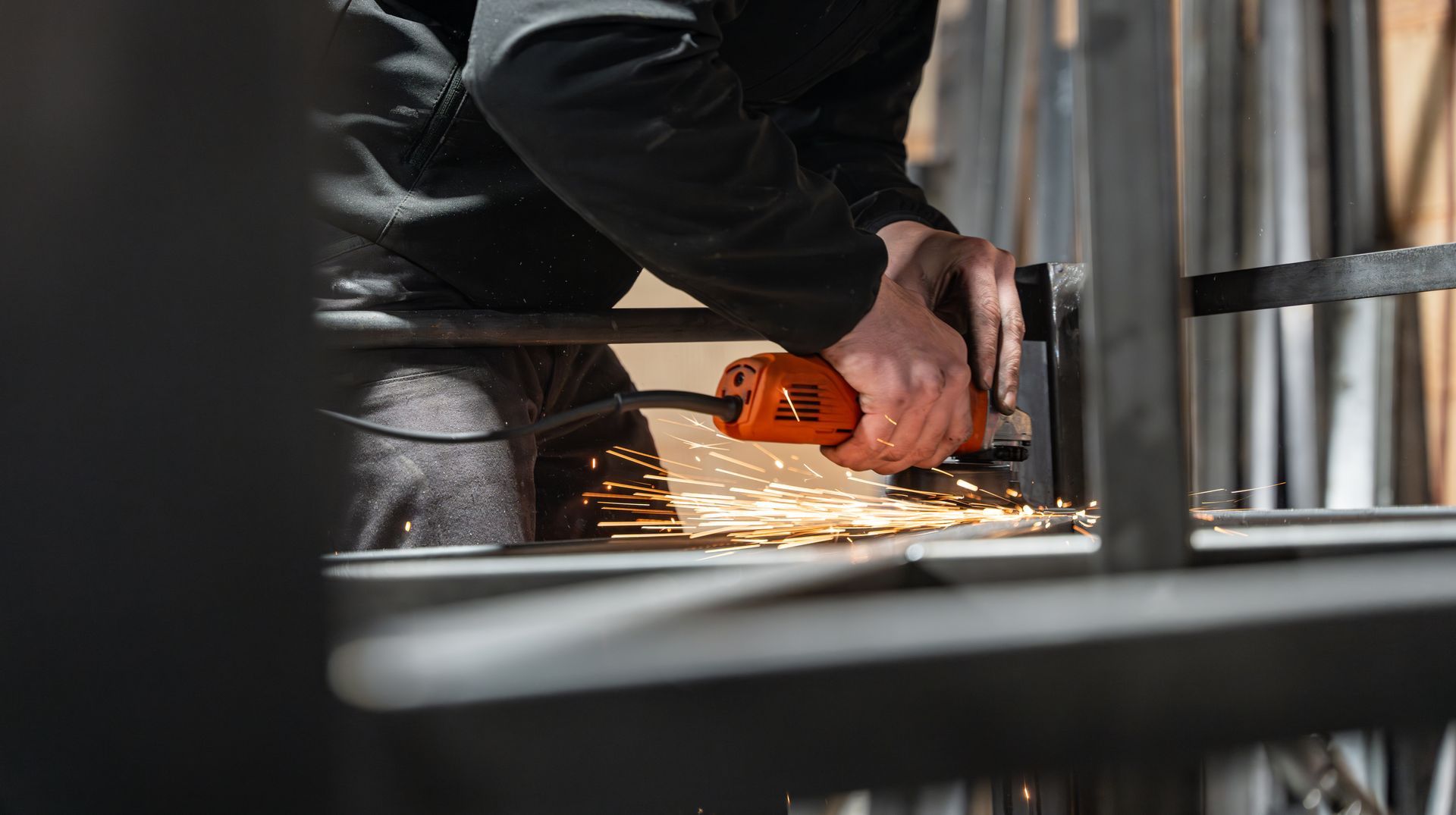 Un ouvrier utilisant une meuleuse d’angle orange, projetant des étincelles dans un environnement industriel.