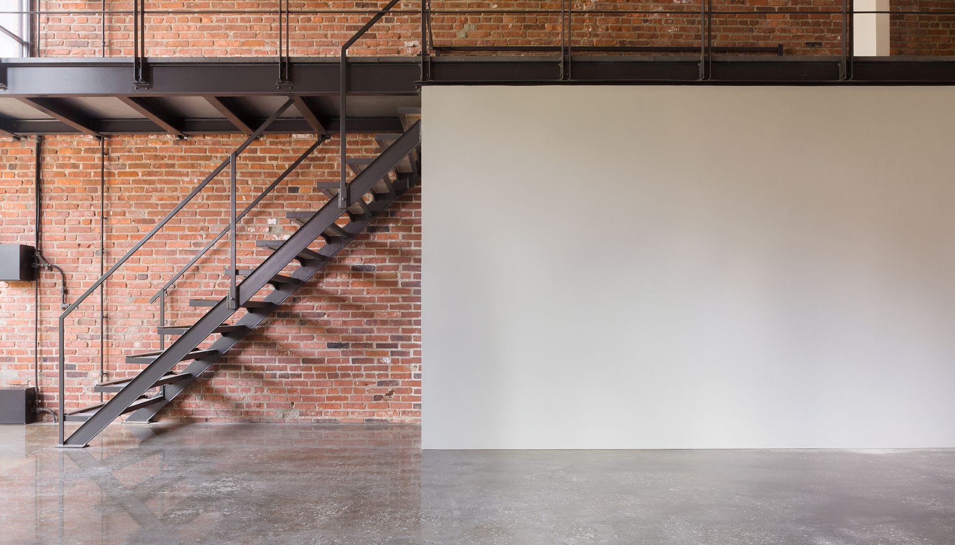 Intérieur de loft industriel avec un mur en briques, un escalier en métal et un grand mur blanc vierge.