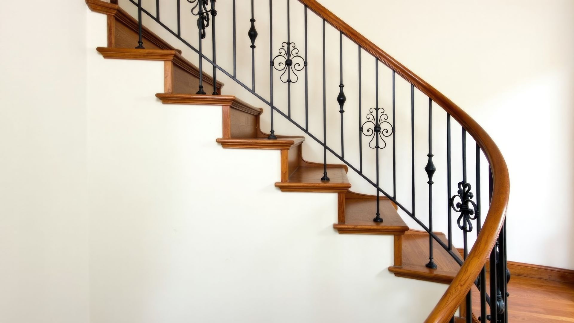 Escalier en bois courbé avec rampe en fer noir dans un intérieur lumineux et blanc