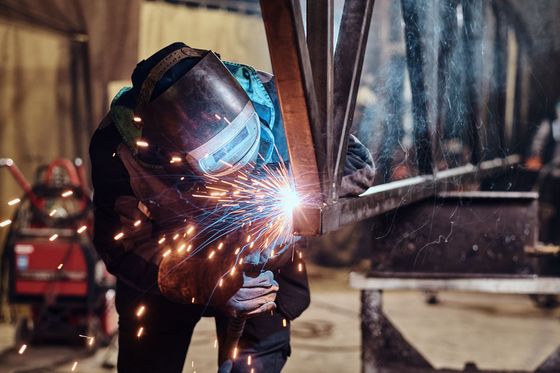 Un soudeur en tenue de protection fait jaillir des étincelles en travaillant le métal dans un atelier industriel.
