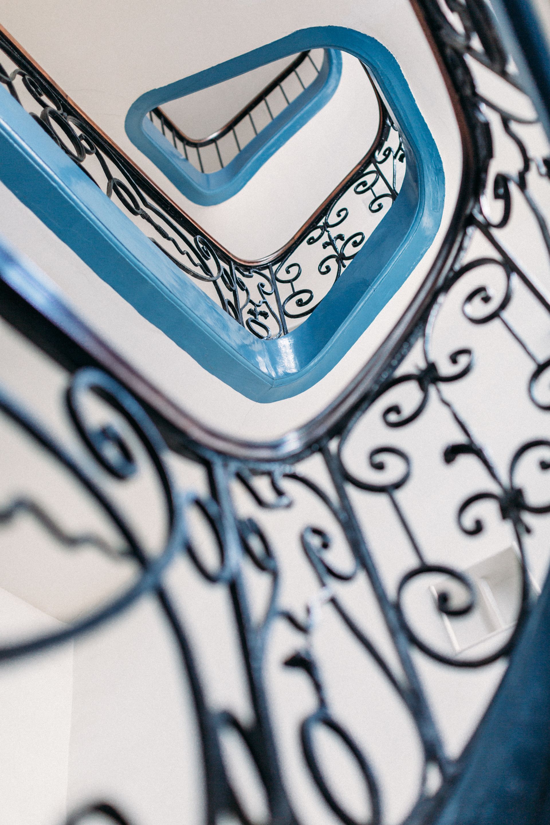 Escalier bleu et blanc avec une rampe décorative en fer forgé noir aux motifs en volutes
