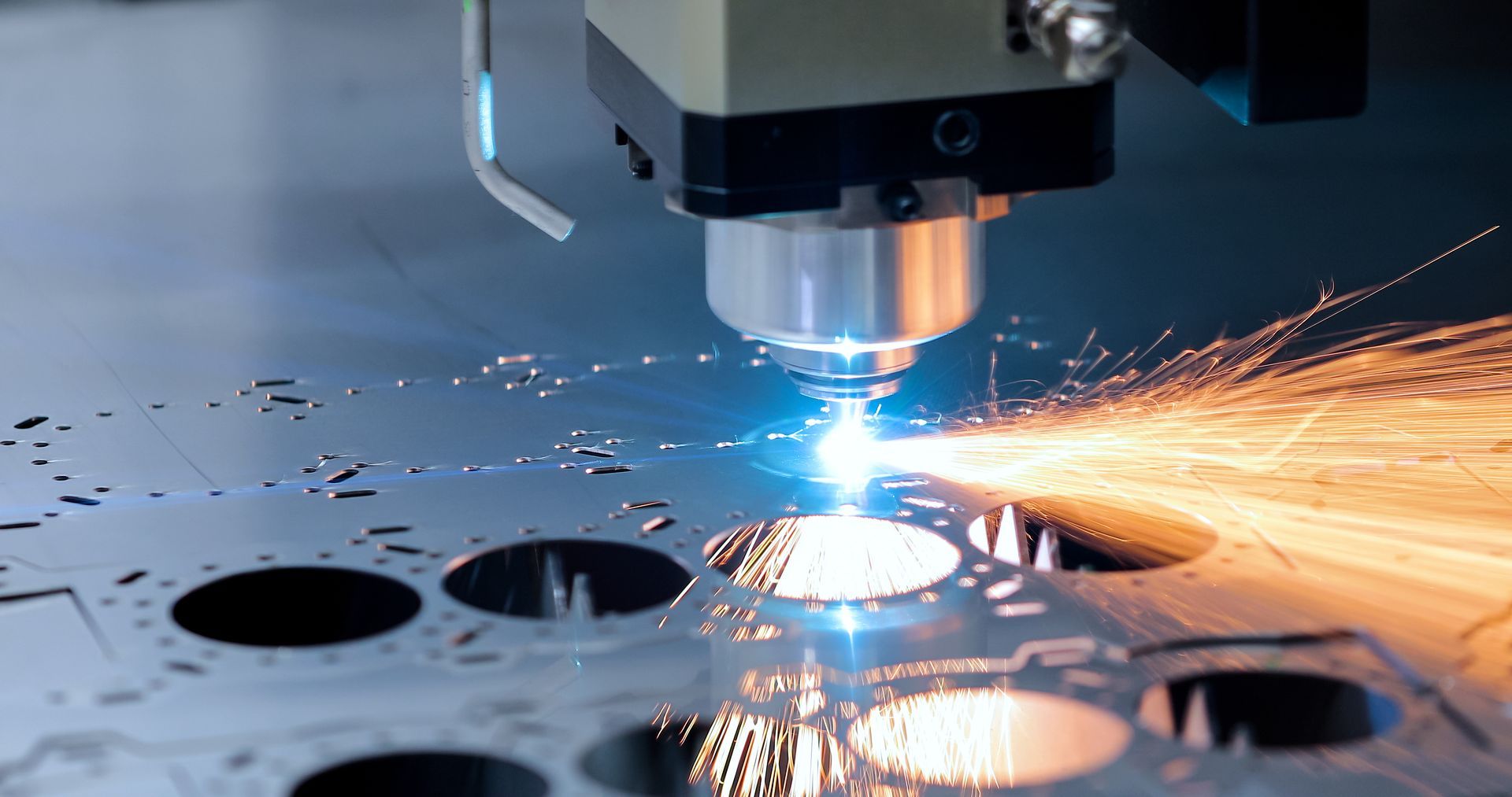Découpe au laser d’une tôle métallique, avec des étincelles brillantes jaillissant de la tête de découpe.