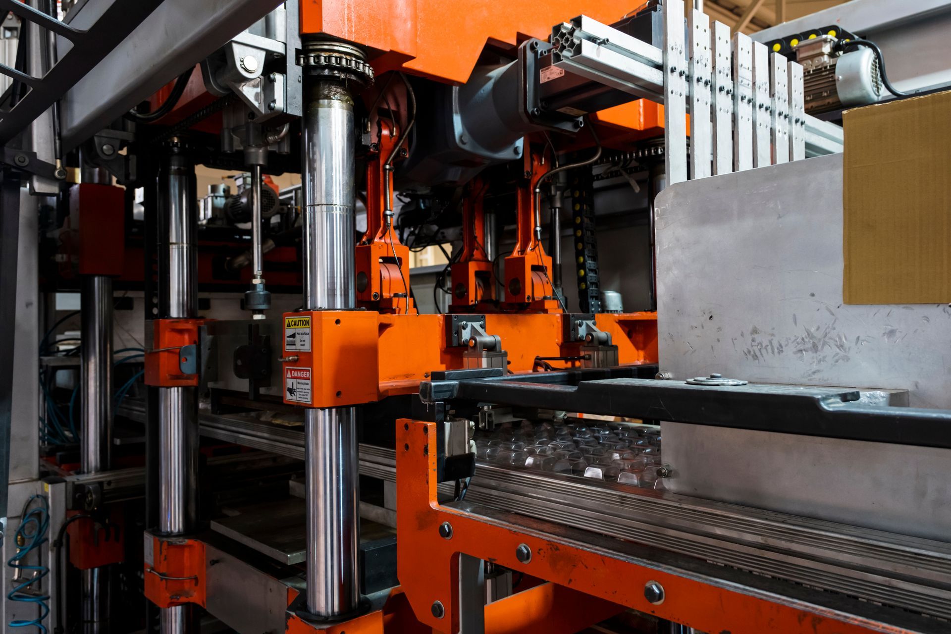 Machine industrielle avec des composants orange et des rouleaux métalliques dans une usine.