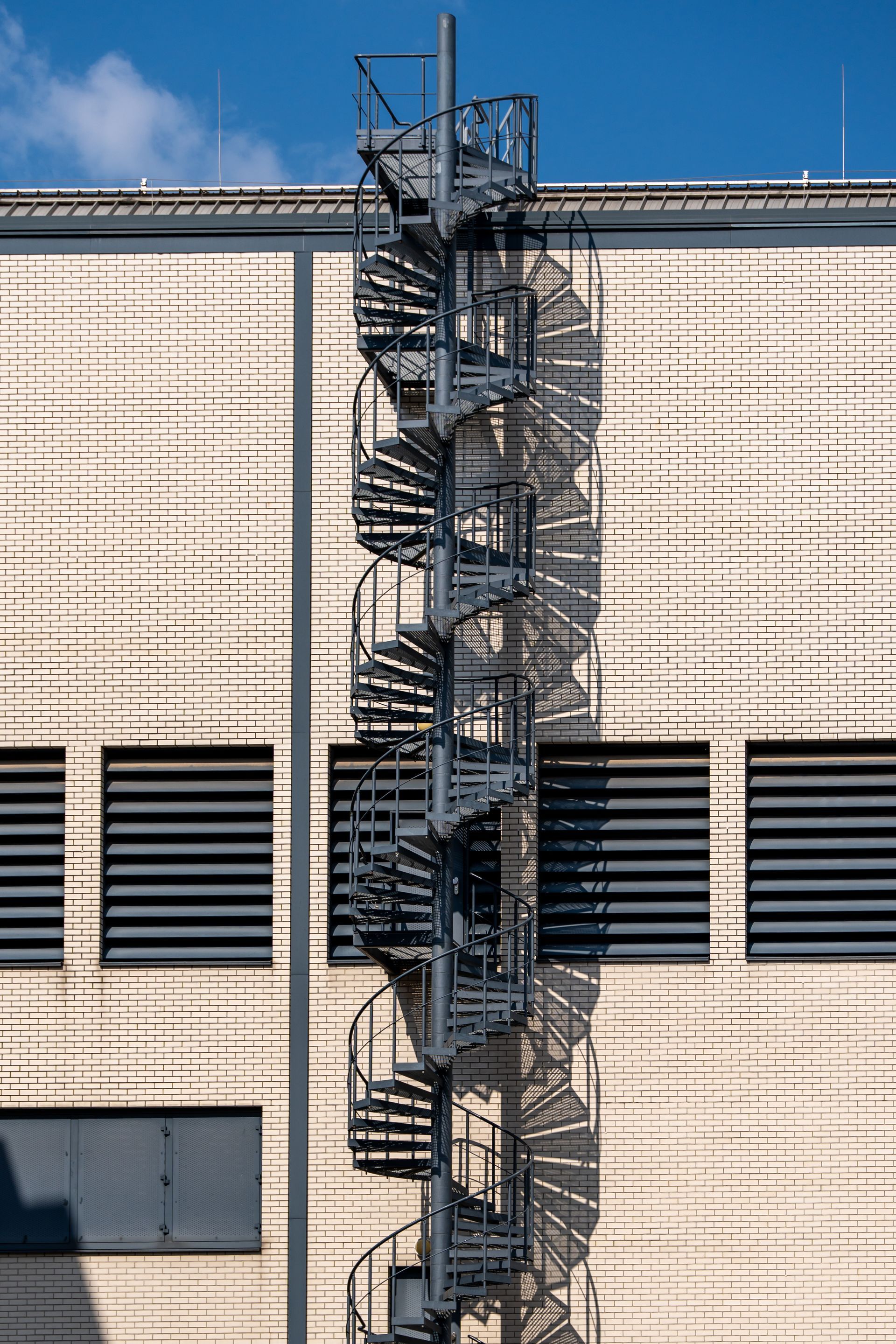 Escalier de secours sur un immeuble en briques beiges, sur fond de ciel bleu