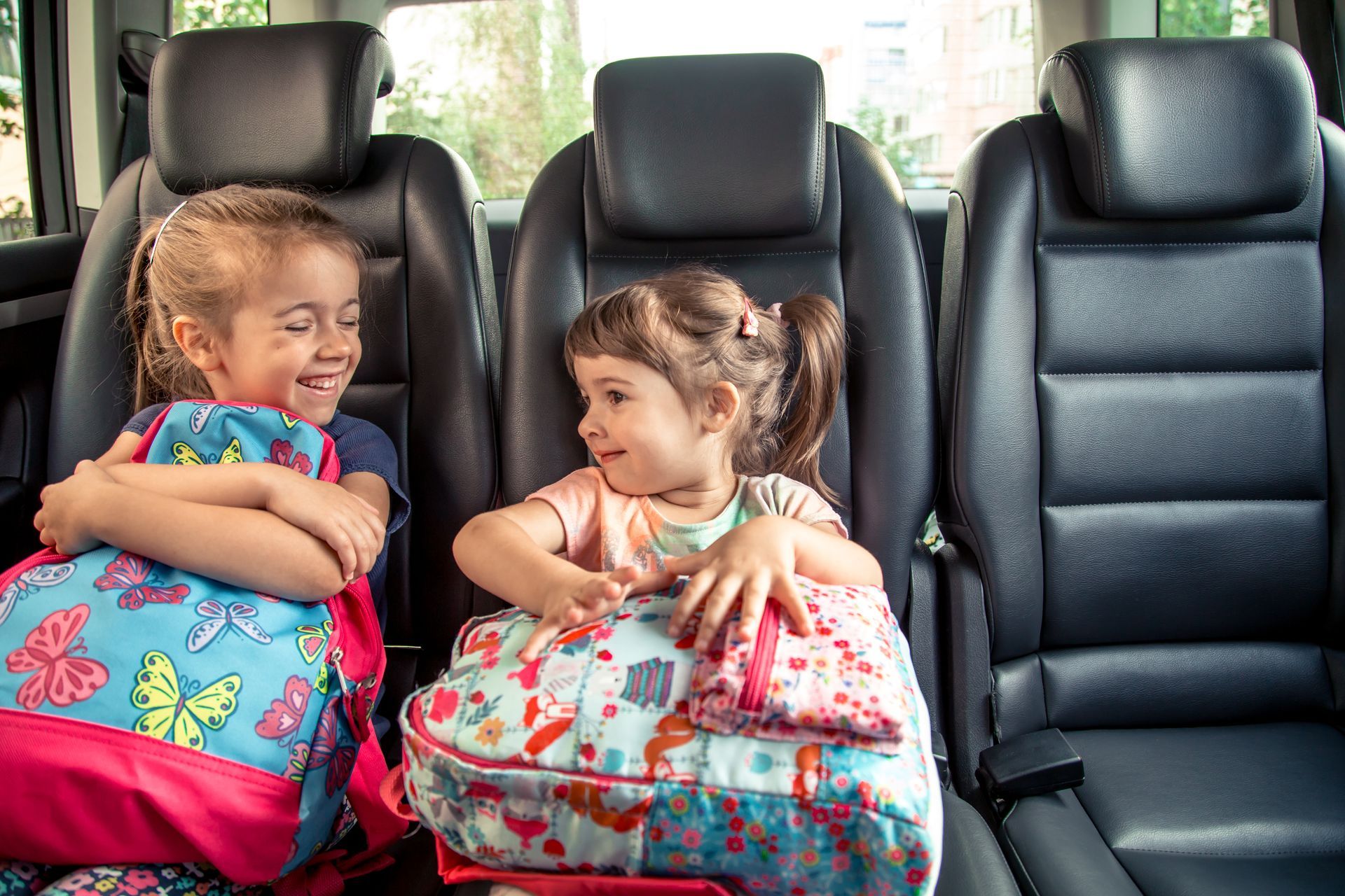 Deux enfants, assis à l'arrière d'une voiture, tiennent des sacs à dos à motifs et se sourient.