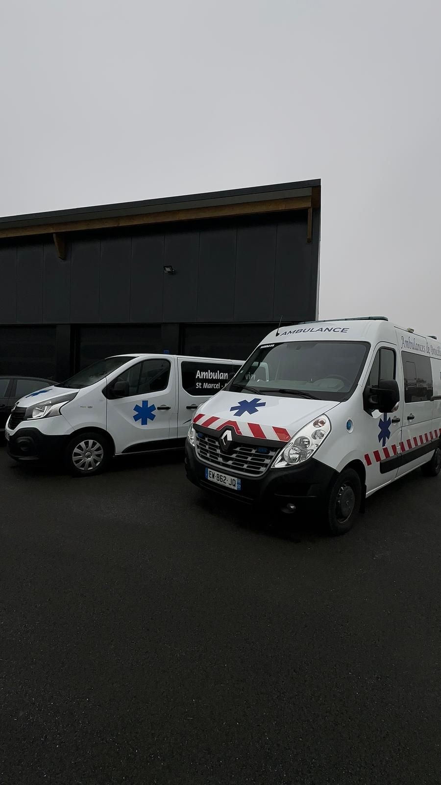 Deux ambulances Renault blanches garées devant un bâtiment sombre par temps couvert.