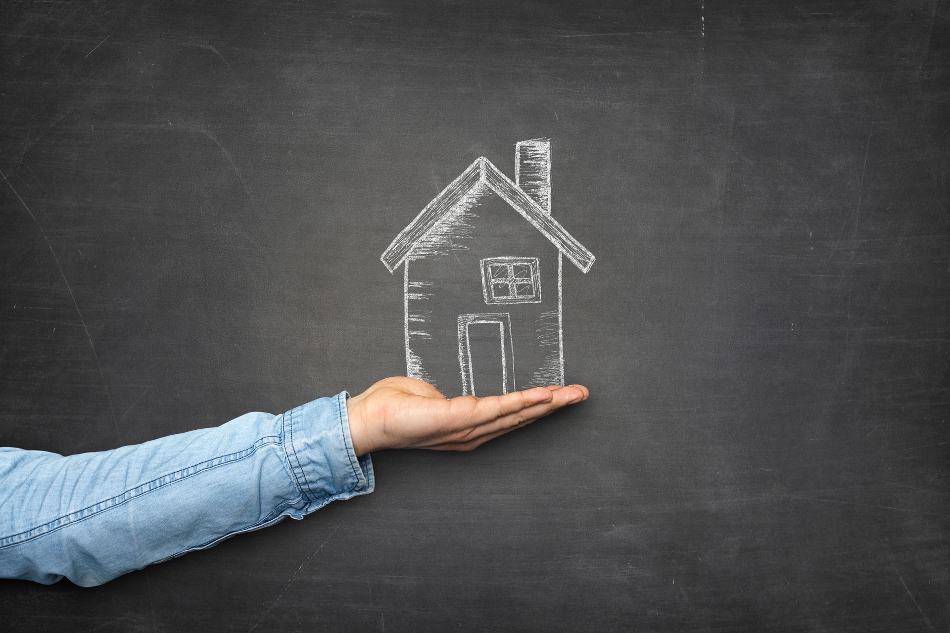 Mano sosteniendo un dibujo con tiza de una casa en una pizarra.