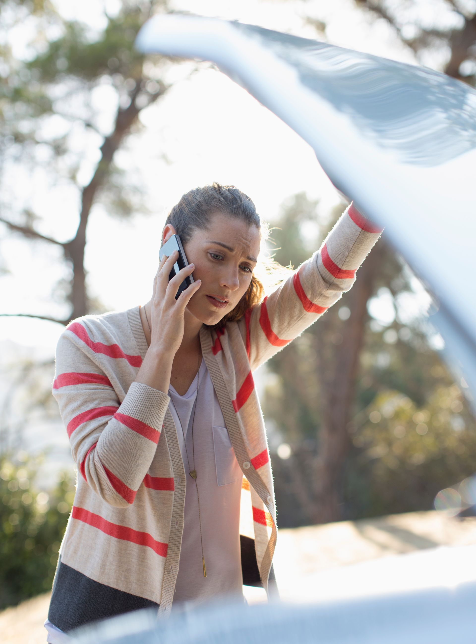 Une femme tenant le capot de son véhicule tient son téléphone portable