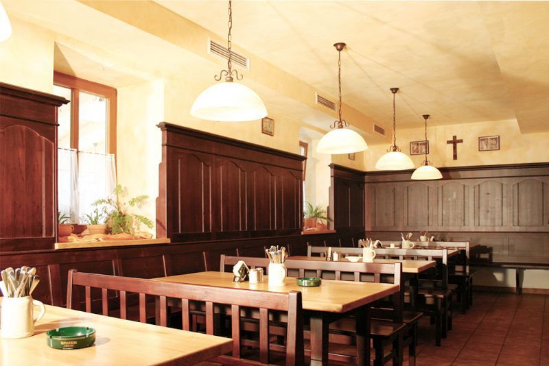 Gemütlicher Gastraum mit Holzmöbeln, Pendelleuchten und dunkler Holzvertäfelung an den Wänden.