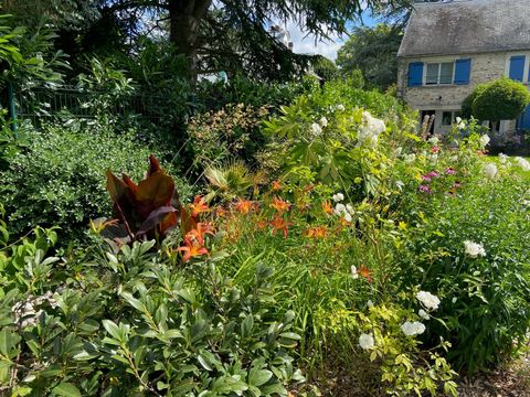 Jardin luxuriant avec des lys orange et des fleurs blanches, devant une maison en pierre aux volets bleus.