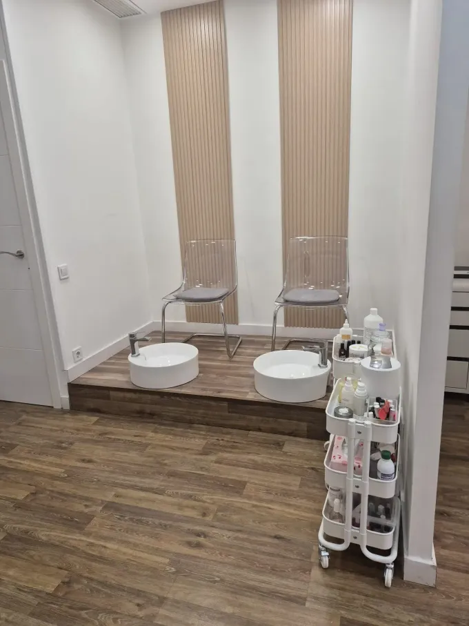 Un puesto de pedicura con dos sillas sobre una plataforma de madera elevada, palanganas blancas para los pies y un carrito blanco con ruedas para los suministros.