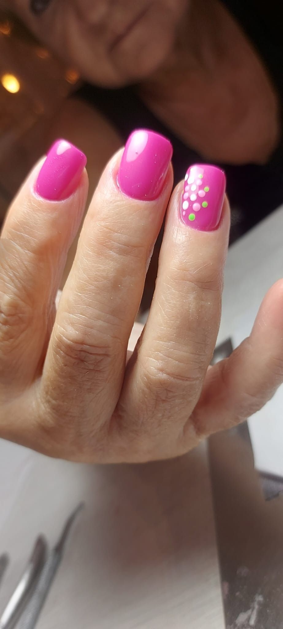 La mano de una persona muestra unas uñas de un rosa vibrante perfectamente cuidadas, con el dedo anular decorado con delicados detalles florales blancos.