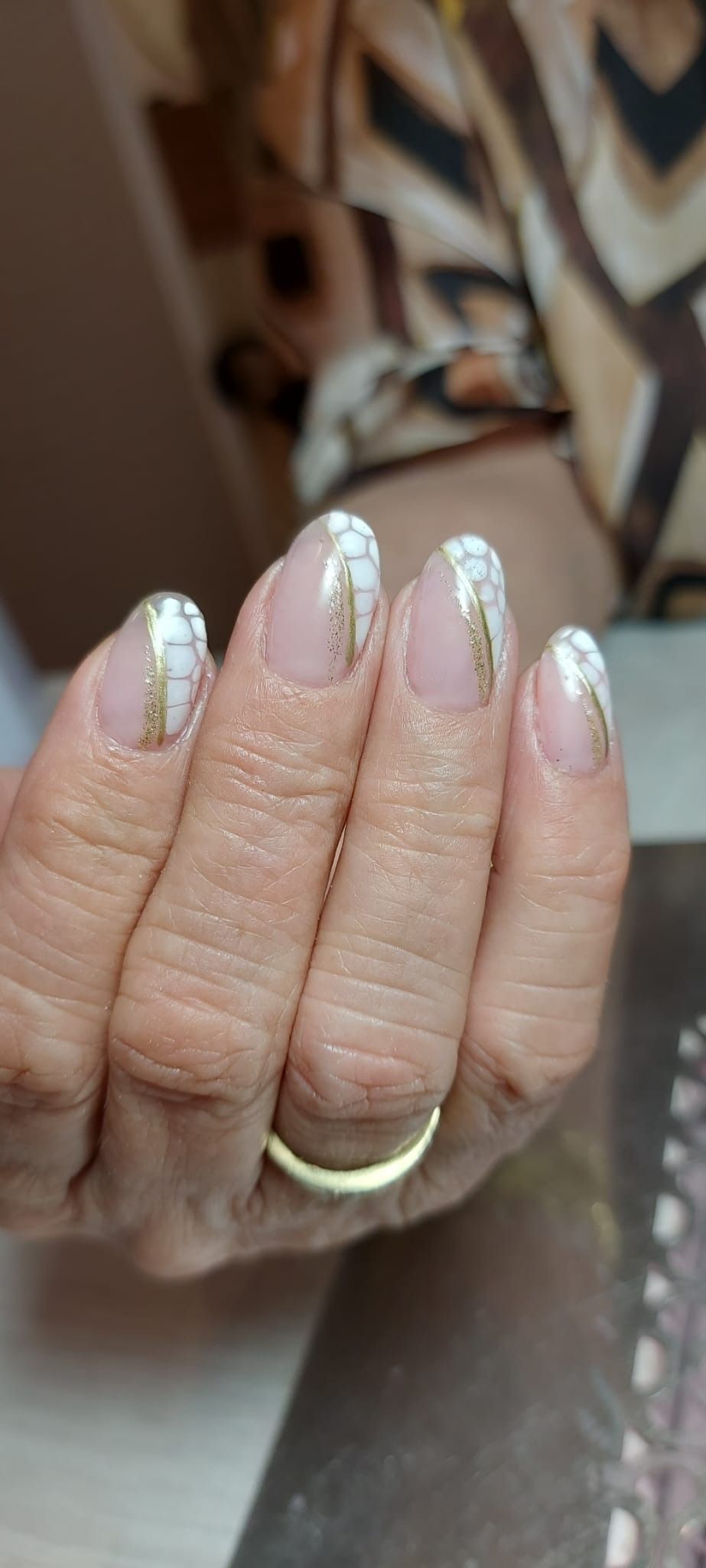 Una mano con uñas almendradas, cuidadosamente arregladas, con una base rosa claro y una línea vertical dorada que las adorna.