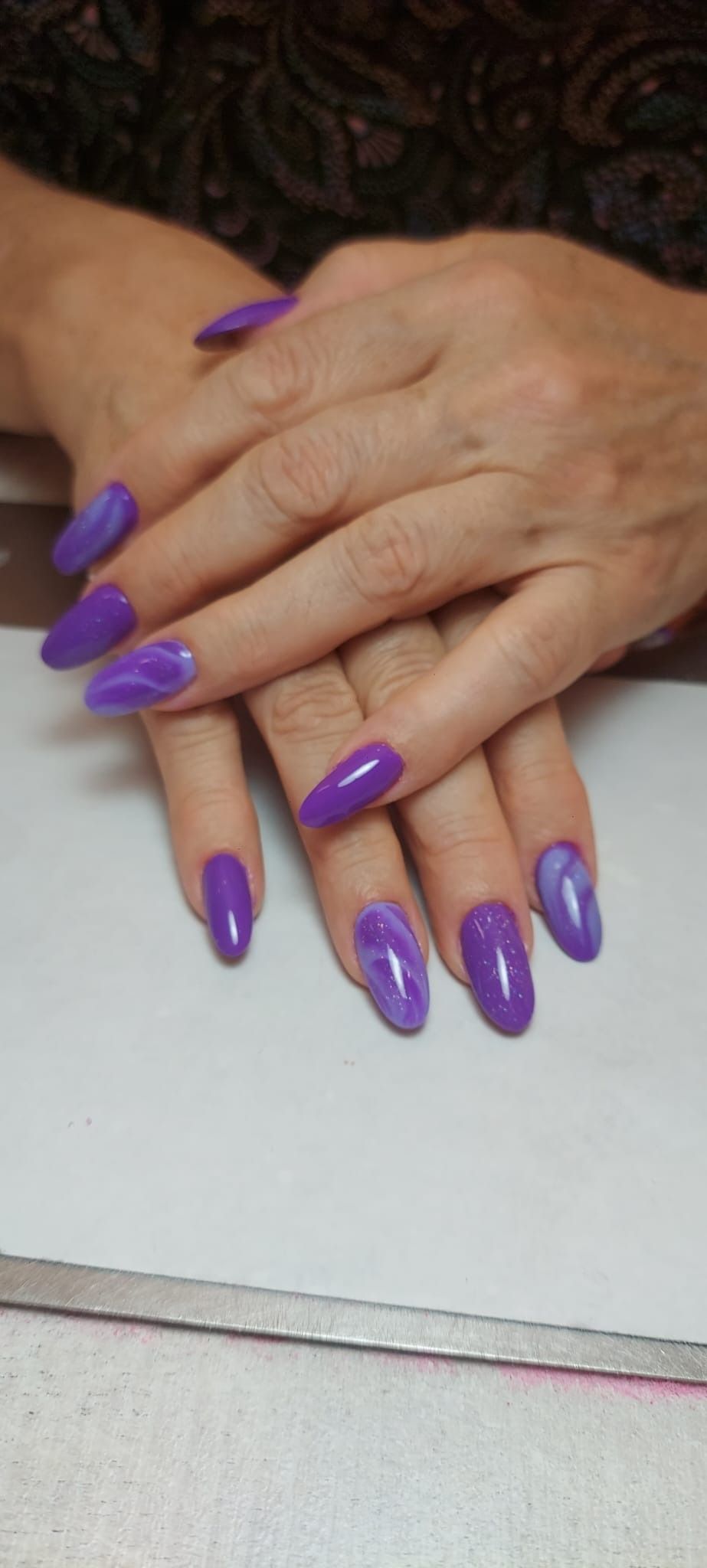 Dos manos con uñas largas y ovaladas pintadas de un color morado brillante, apoyadas una sobre la otra.