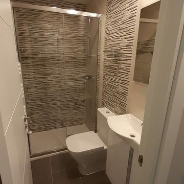 Un baño con inodoro, lavabo, ducha y espejo.