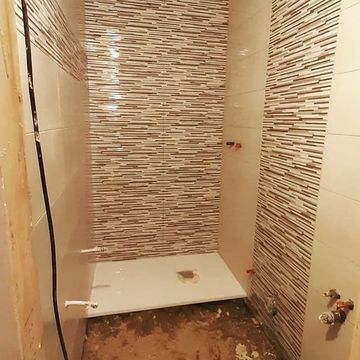 Un baño en construcción con pared de azulejos y cabina de ducha.