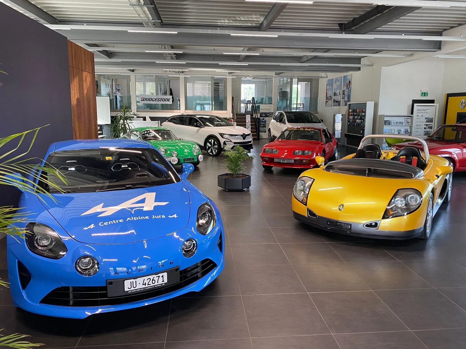 Une voiture bleue est garée dans une salle d'exposition à côté d'une voiture jaune.