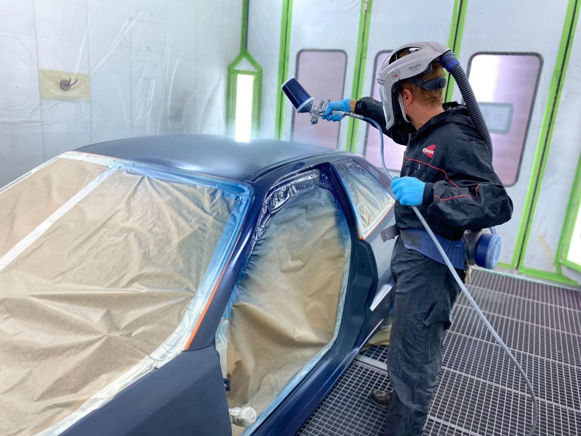 Un homme peint une voiture au pistolet dans une cabine de peinture.