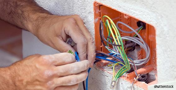 Mains connectant des câbles électriques colorés à l'intérieur d'une boîte orange dans un mur.
