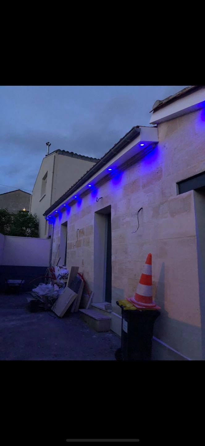 Extérieur d'un bâtiment avec des lumières bleues sur le toit. Un cône de chantier est posé près d'une poubelle.
