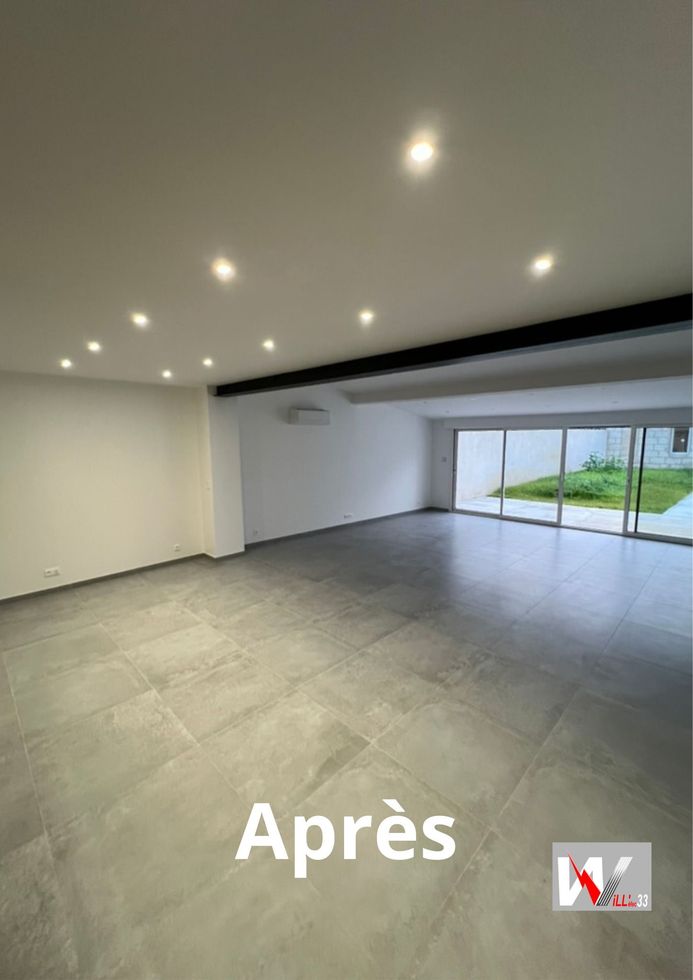 Chambre vide et moderne avec sol carrelé gris, murs blancs, lumières encastrées et portes coulissantes en verre donnant sur un petit jardin.