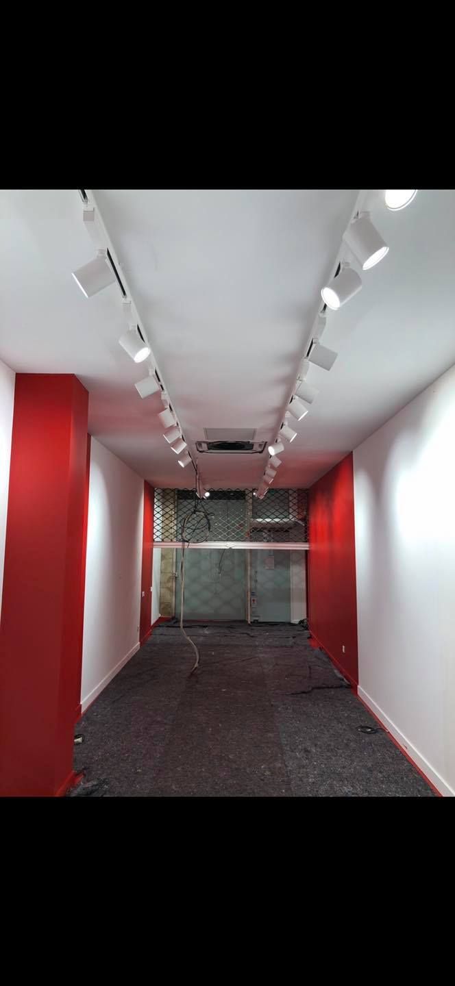 Espace commercial vide, murs blancs avec piliers rouges, éclairage sur rail au plafond, vitrine en verre.