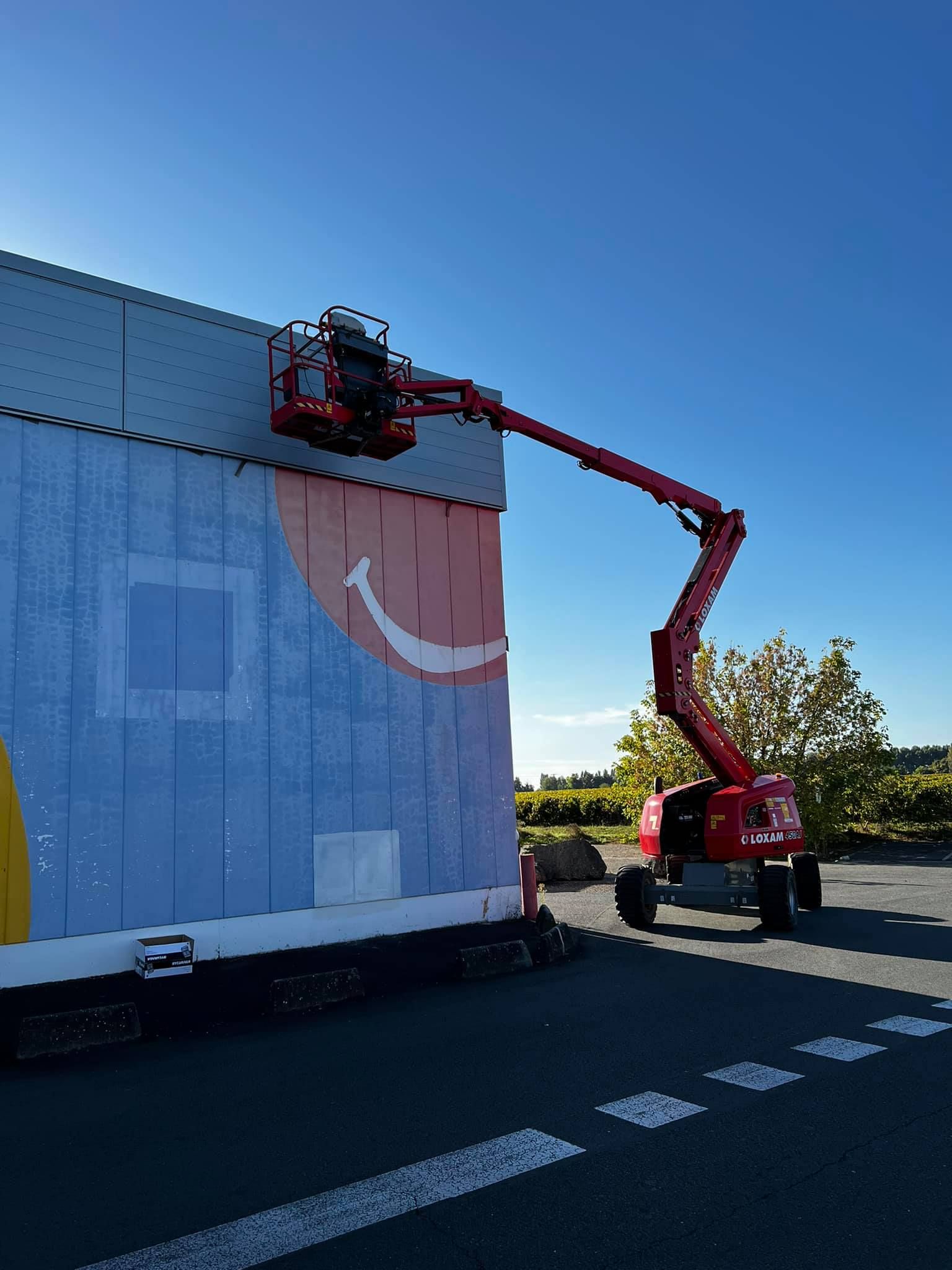 Ascenseur rouge atteignant un bâtiment bleu orné d'un sourire. Ciel bleu clair.