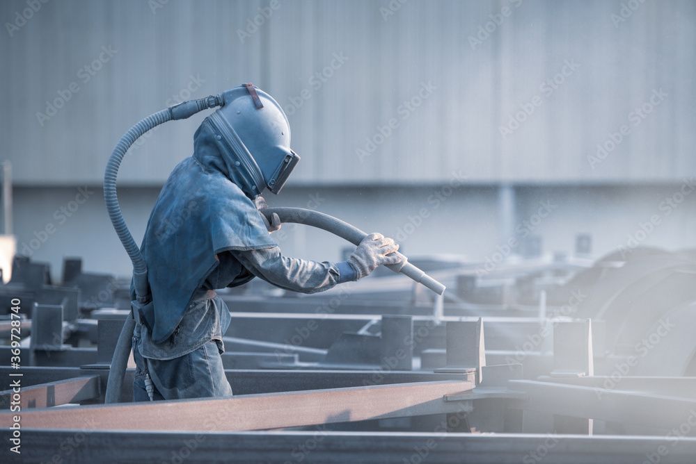 Ein Mann sandstrahlt in einer Fabrik ein Stück Metall.