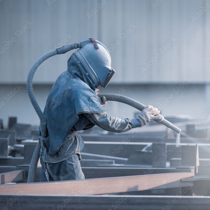 Ein Mann sandstrahlt eine Metallstruktur in einer Fabrik.