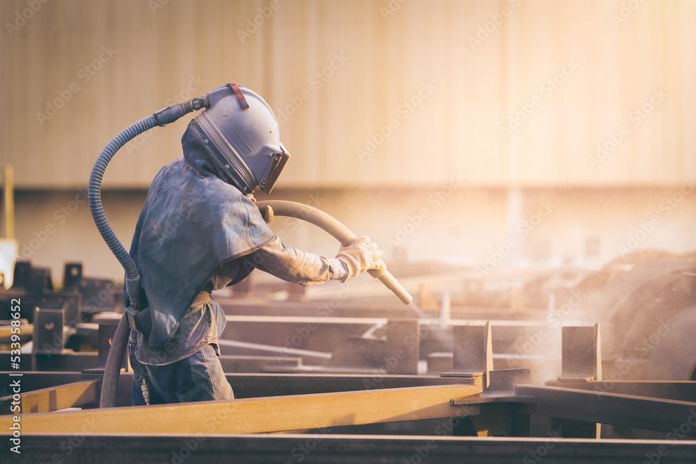 Ein Mann sandstrahlt eine Metallstruktur in einer Fabrik.