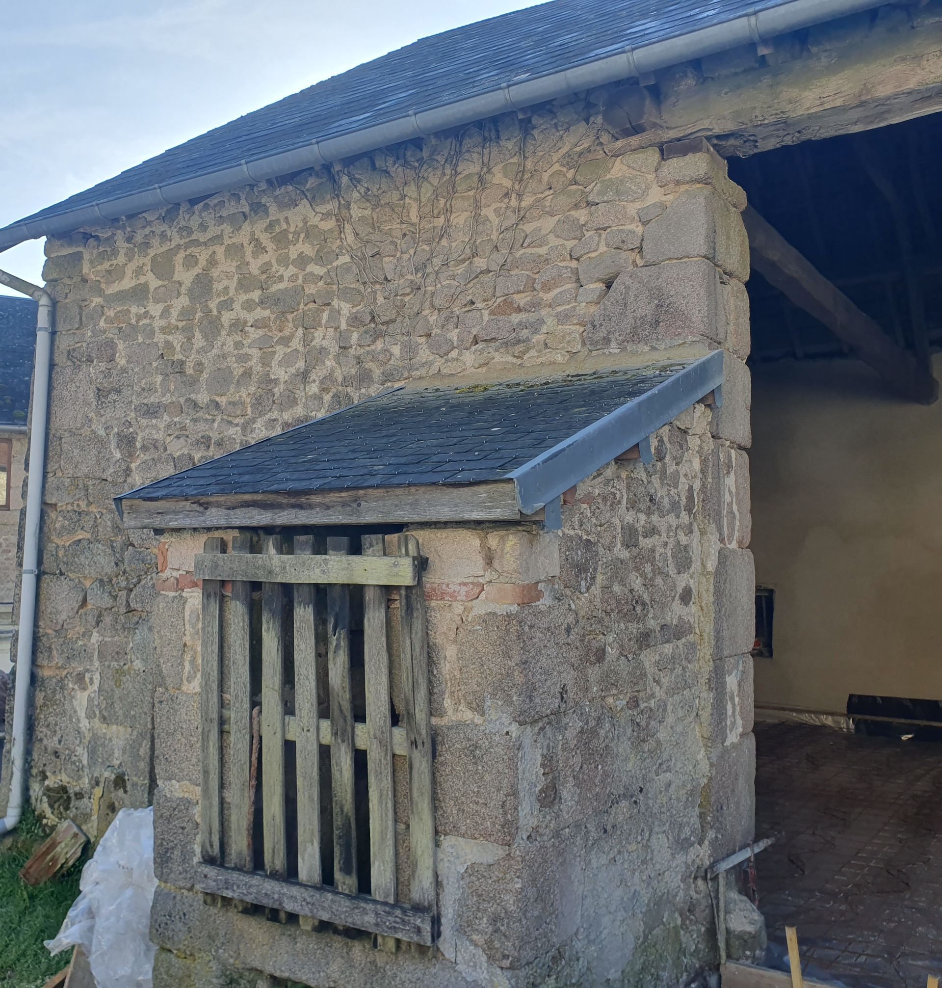 Mur de grange en pierre avec un petit abri au toit incliné