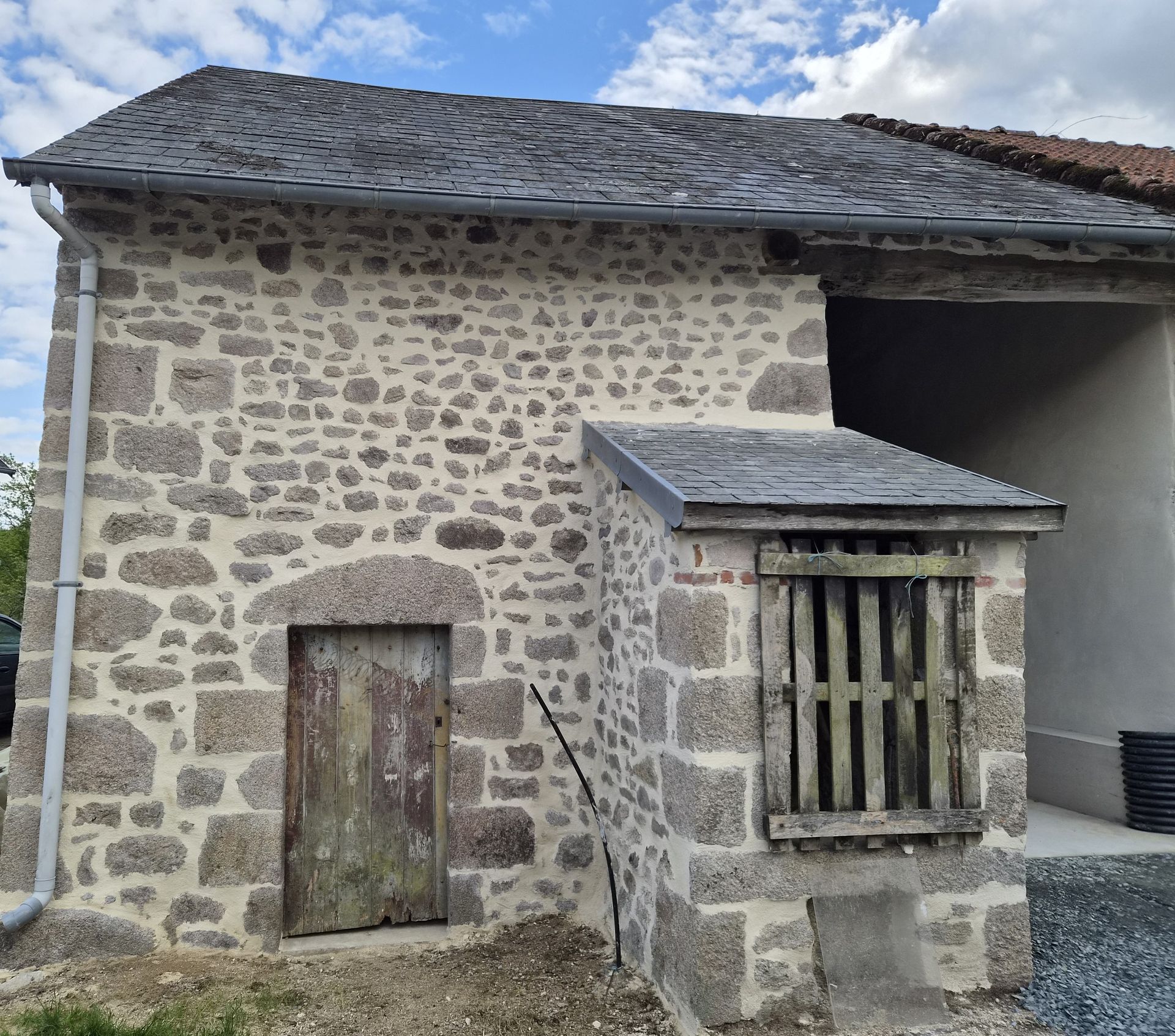 Bâtiment en pierre avec toit d'ardoise grise, petite porte en bois et fenêtre à barreaux