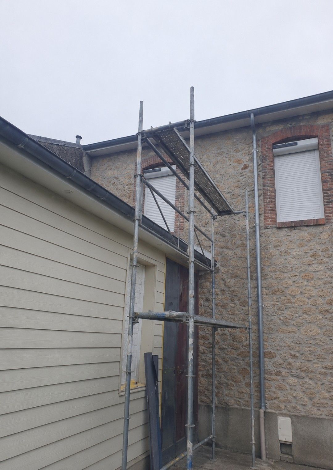 Échafaudages à côté d'un bâtiment en briques beiges et d'un bardage blanc