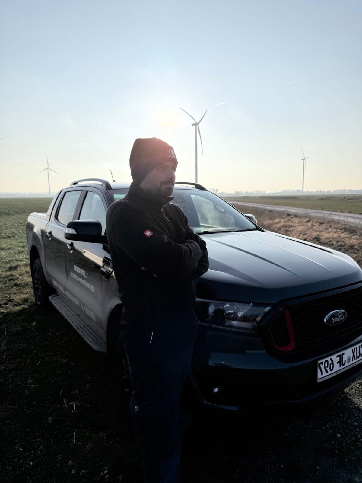 Ein Mann steht neben einem Anhänger und einem LKW.