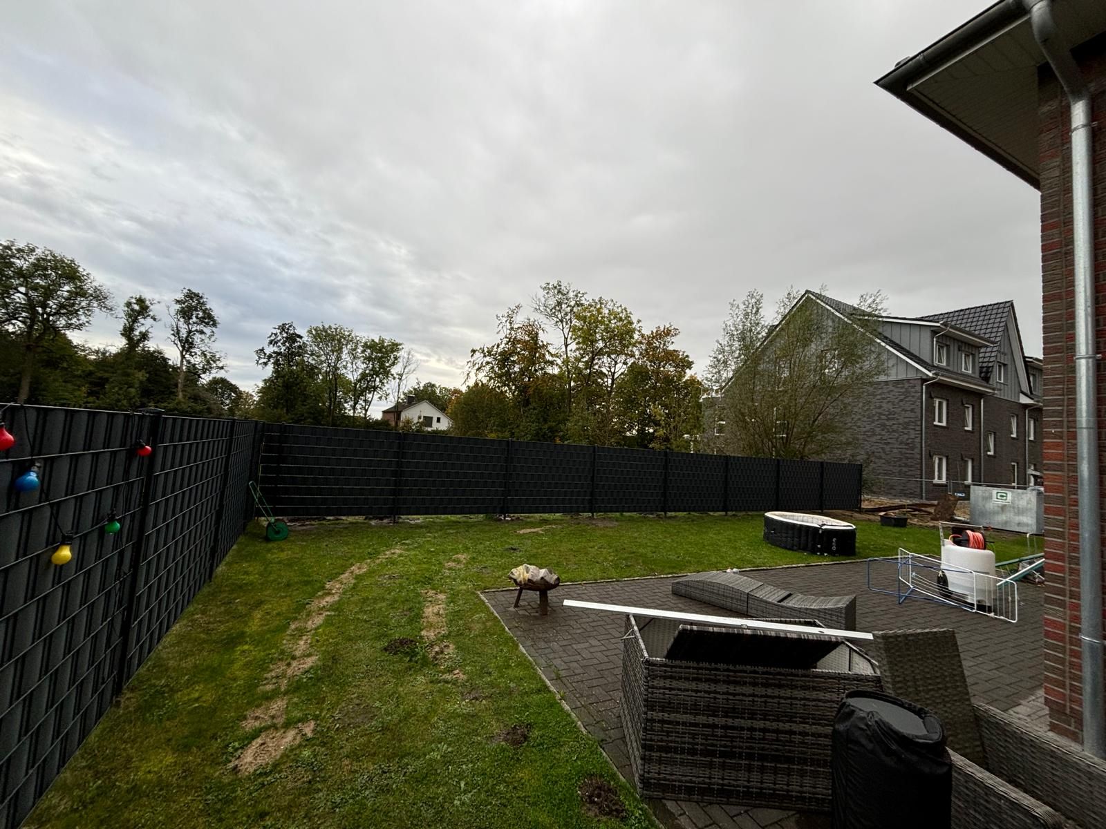 Ein Hinterhof mit einem schwarzen Zaun und einem Backsteingebäude im Hintergrund.