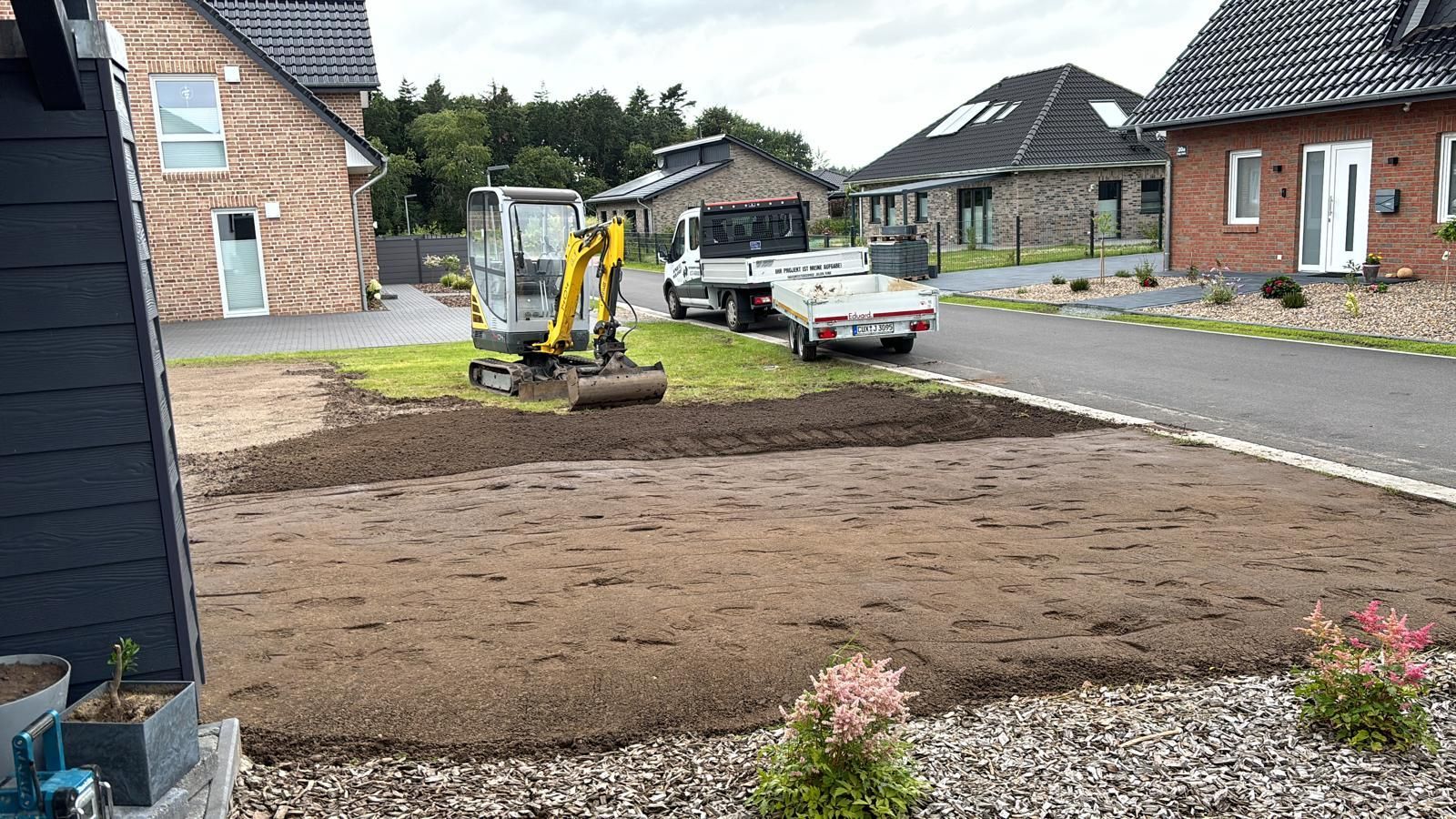 Ein kleiner Bagger arbeitet auf einem Rasen vor einem Haus.