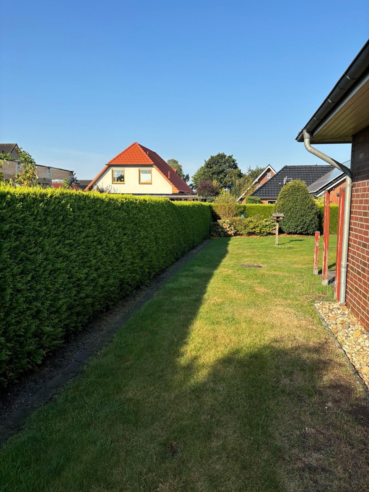 Ein üppig grüner Garten mit einem Backsteinhaus im Hintergrund.