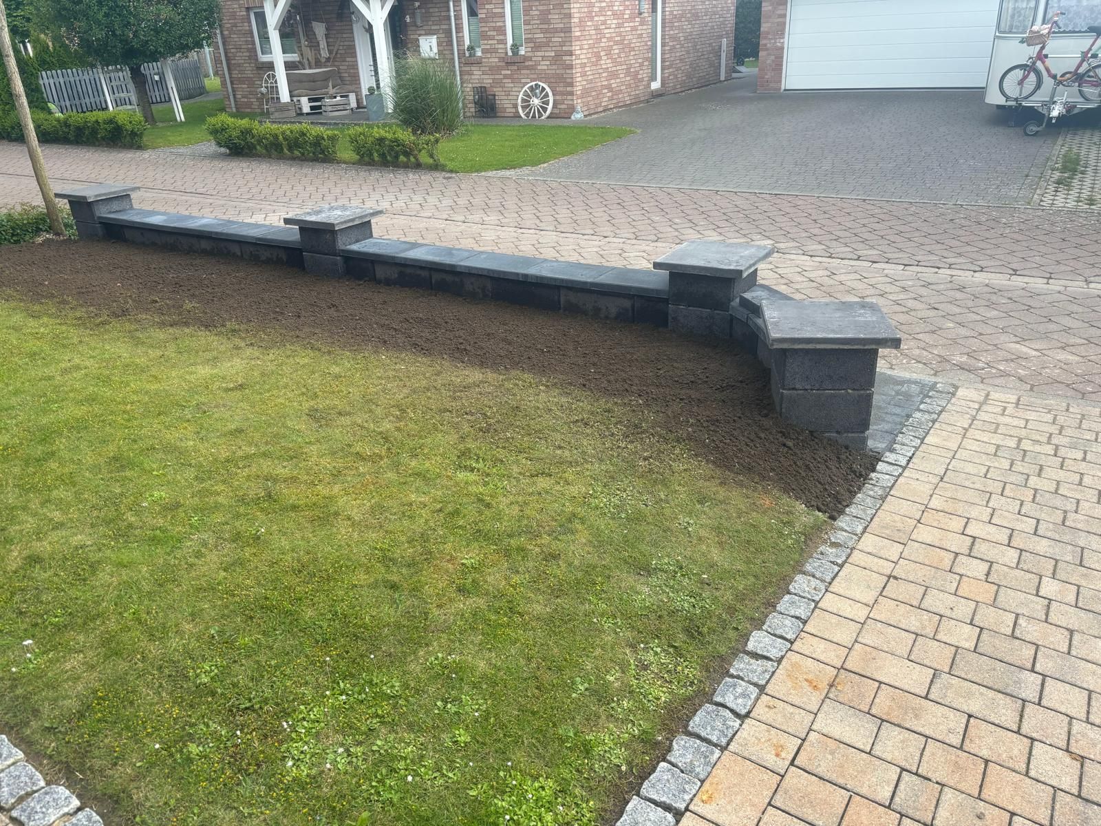 Ein Backsteinweg führt zu einem Haus, davor steht eine Backsteinmauer.